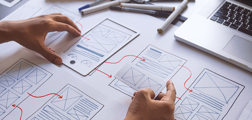 Hands arranging website wireframes beside a laptop